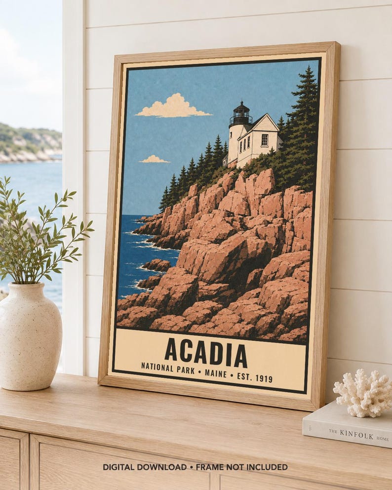 May include: A framed travel poster print featuring a lighthouse perched on rocky cliffs above a blue ocean, with evergreen trees and a light blue sky. The text at the bottom reads ACADIA NATIONAL PARK MAINE EST. 1919 in bold black lettering.