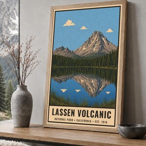 K&ouml;nnte beinhalten: Ein gerahmter Kunstdruck mit einer Landschaftsillustration des Lassen Volcanic Nationalparks in Kalifornien. Das Bild zeigt einen Berggipfel, der sich in einem See spiegelt, umgeben von Kiefern, mit dem Text Lassen Volcanic National Park California Est. 1916.