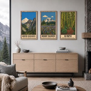 Op de afbeelding: Drie verticale wandkunstprints met illustraties van de nationale parken North Cascades, Mount Rainier en Olympic. Elke print toont een landschap met bergen, bossen of wilde bloemen, inclusief de naam van het park en bijbehorende tekst.