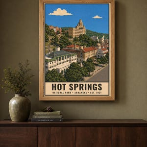 Może przedstawiać: Oprawiony pionowy plakat przedstawiający Park Narodowy Hot Springs w Arkansas. Ilustracja przedstawia zabytkowe budynki, bujne zielone drzewa i bezchmurne niebieskie niebo z chmurami. Tekst głosi HOT SPRINGS NATIONAL PARK ARKANSAS EST. 1921.