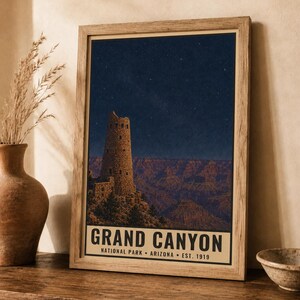 May include: A framed vertical poster featuring a night scene of the Grand Canyon with the Desert View Watchtower under a starry sky. The text at the bottom reads GRAND CANYON NATIONAL PARK ARIZONA EST. 1919. The print is in a light wood frame.
