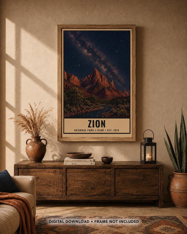 May include: A rectangular wall art print featuring a night landscape of Zion National Park with red rock mountains under a starry sky and the text ZION NATIONAL PARK UTAH EST. 1919. The print is displayed in a wooden frame on a beige wall.