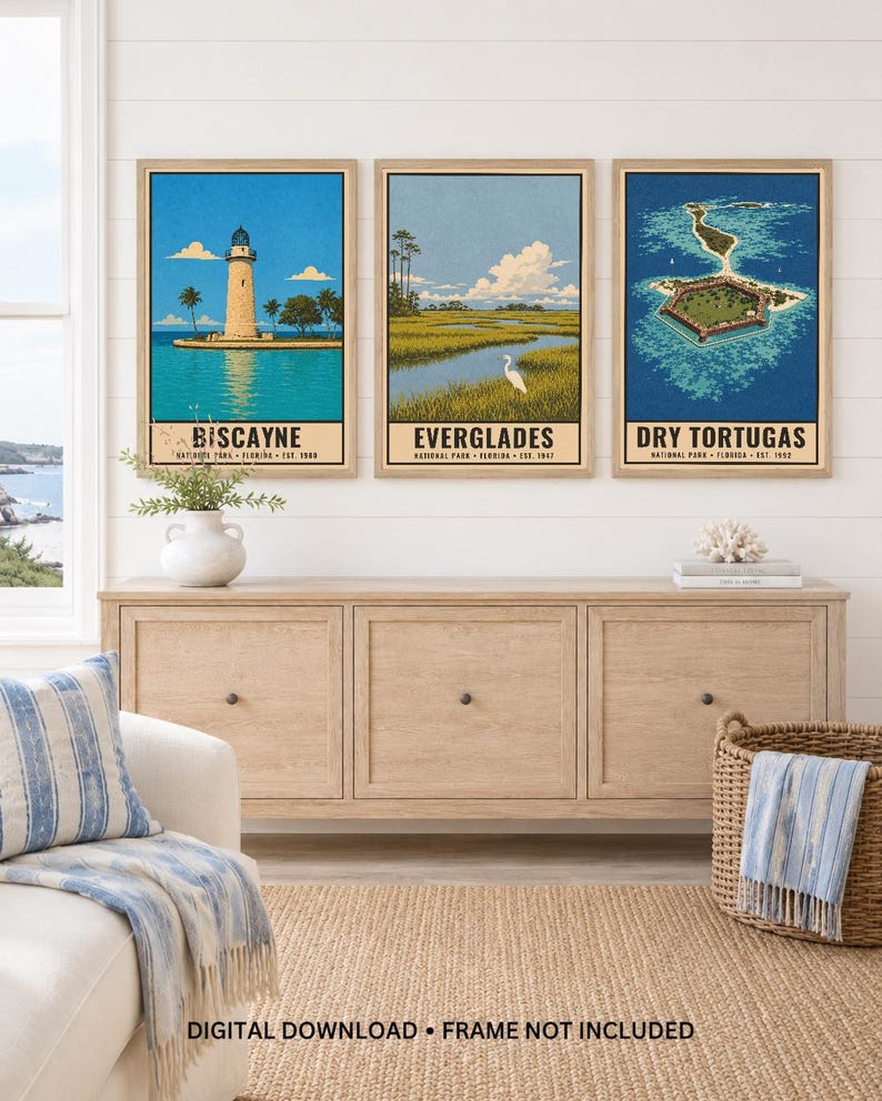 May include: Three framed vertical wall art prints featuring illustrations of Florida national parks. The left print shows the Biscayne lighthouse, the center print depicts the Everglades wetlands with a white bird, and the right print shows Dry Tortugas.