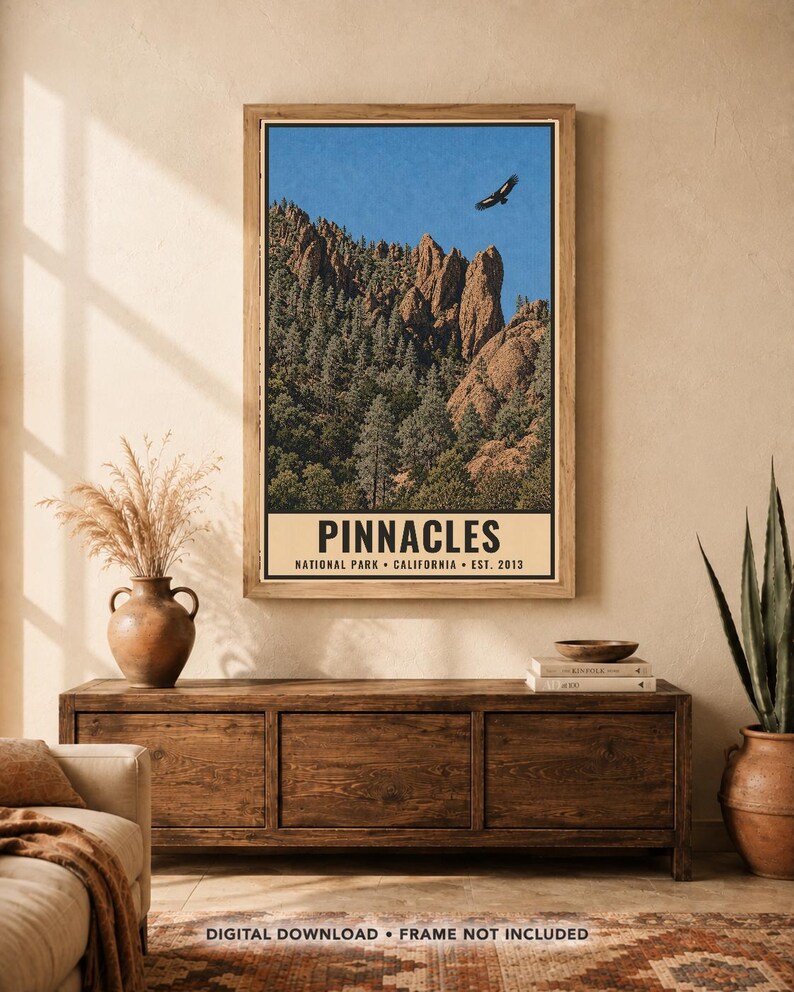 Op de afbeelding: Een verticale poster met een landschap van Pinnacles National Park met rotsachtige kliffen, dennenbomen en een vogel die in een blauwe lucht vliegt. Het onderste gedeelte heeft een cr&egrave;mekleurige rand met de tekst PINNACLES NATIONAL PARK CALIFORNIA EST. 2013.