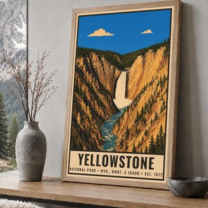 Op de afbeelding: Een ingelijste verticale poster met een gestileerde illustratie van een waterval die door een diepe kloof met dennenbomen stroomt, onder een helderblauwe lucht met twee wolken. De tekst luidt YELLOWSTONE NATIONAL PARK WYO., MONT. & IDAHO EST. 1872.