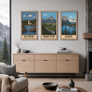 Op de afbeelding: Drie verticale ingelijste kunstprints van de nationale parken Isle Royale, Grand Teton en Glacier. Elke print toont een landschapsillustratie met blauwe luchten, bergen, bossen en water, met de parknaam onderaan de afbeelding.