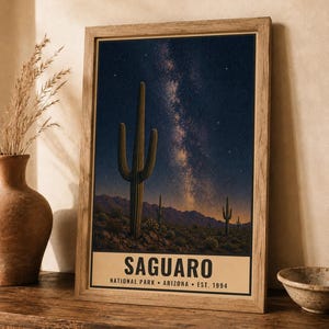 Puede incluir: Una l&aacute;mina de arte mural vertical enmarcada que muestra un cielo nocturno con la V&iacute;a L&aacute;ctea sobre un paisaje des&eacute;rtico con cactus saguaro y monta&ntilde;as. La parte inferior contiene el texto SAGUARO NATIONAL PARK ARIZONA EST. 1994 en letras negras.