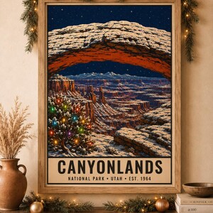 May include: A framed vertical poster of Canyonlands National Park in Utah, featuring a snow-covered rock arch over a canyon landscape at night under a starry sky, with a small evergreen tree decorated with colorful lights in the foreground.