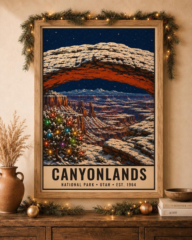 May include: A framed vertical poster of Canyonlands National Park in Utah, featuring a snow-covered rock arch over a canyon landscape at night under a starry sky, with a small evergreen tree decorated with colorful lights in the foreground.