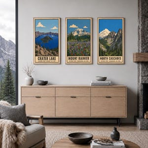Op de afbeelding: Drie verticale rechthoekige wandposters in houten lijsten met illustraties van de nationale parken Crater Lake, Mount Rainier en North Cascades. Elke print toont de naam van het park, de locatie en het oprichtingsjaar in zwarte tekst.
