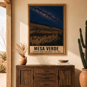 May include: A rectangular wall poster featuring a night sky filled with stars above the cliff dwellings of Mesa Verde National Park in Colorado. The text reads MESA VERDE NATIONAL PARK COLORADO EST. 1906 in bold black letters on a beige background.