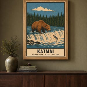 Pu&ograve; includere: Una stampa da parete incorniciata raffigurante un orso bruno al bordo di una cascata che cattura un pesce che salta. La scena include uno sfondo boschivo e un cielo blu. Il testo recita KATMAI NATIONAL PARK ALASKA EST. 1980 in basso.