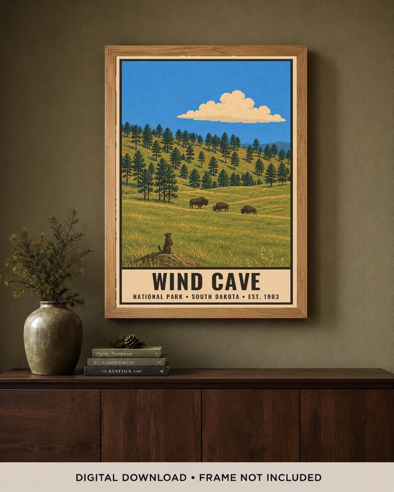 May include: A framed poster featuring a landscape illustration of Wind Cave National Park in South Dakota. The artwork depicts a grassy hillside with pine trees, three bison, and a prairie dog, under a blue sky with a single cloud. Text reads WIND CAVE.