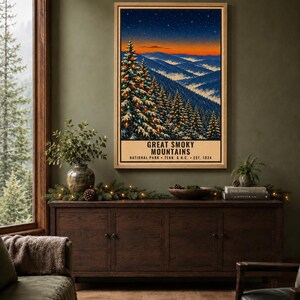 May include: A vertical rectangular poster in a light wood frame depicting the Great Smoky Mountains National Park at twilight. The artwork features snow-covered pine trees with colorful lights, a starry sky, and the text Great Smoky Mountains National Park Tenn. & N.C. Est. 1934.
