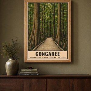 May include: A rectangular wall art print featuring a forest scene with tall trees and a wooden boardwalk path. The text at the bottom reads CONGAREE NATIONAL PARK SOUTH CAROLINA EST. 2003. The print is displayed in a light wood frame on a wall.