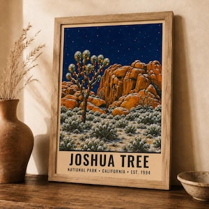 May include: A framed art print featuring a night scene of Joshua Tree National Park with a starry sky, orange rock formations, and a Joshua tree decorated with lights. The text reads JOSHUA TREE NATIONAL PARK CALIFORNIA EST. 1994.
