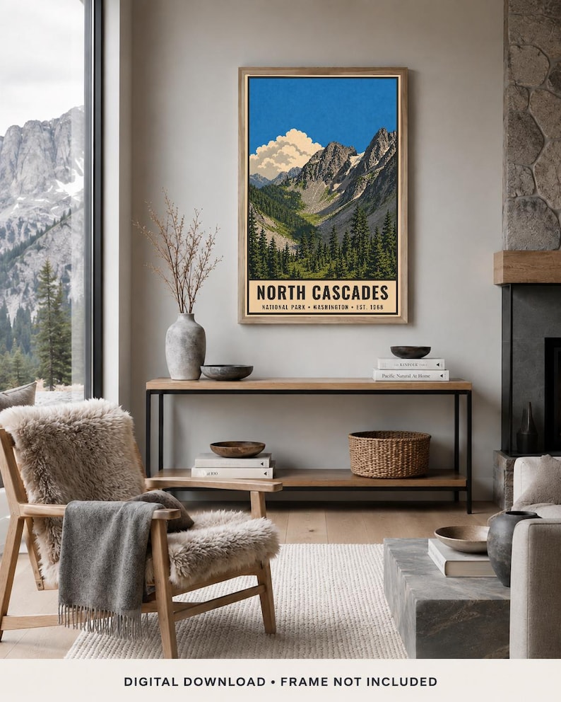 Op de afbeelding: Een ingelijste verticale wandkunstprint van het North Cascades National Park in Washington, opgericht in 1968. De illustratie toont grillige bergtoppen, een helderblauwe lucht met witte wolken en een dicht bos met groene dennenbomen.