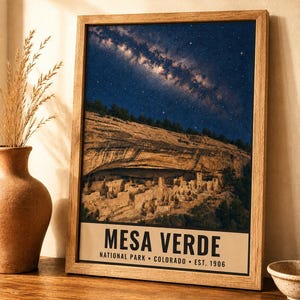 May include: A framed wall art print featuring a night sky filled with stars above the cliff dwellings of Mesa Verde National Park. The print includes the text MESA VERDE NATIONAL PARK COLORADO EST. 1906 in a clean, black sans-serif font at the bottom.