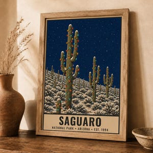 May include: A framed poster featuring a night scene of Saguaro cacti in a desert landscape, decorated with colorful string lights under a starry sky. The text at the bottom reads SAGUARO NATIONAL PARK ARIZONA EST. 1994 in bold black lettering.