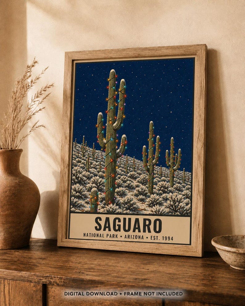 May include: A framed poster featuring a night scene of Saguaro cacti in a desert landscape, decorated with colorful string lights under a starry sky. The text at the bottom reads SAGUARO NATIONAL PARK ARIZONA EST. 1994 in bold black lettering.