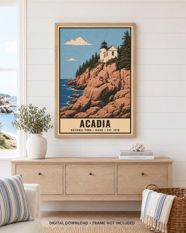 May include: A framed vertical art print featuring a lighthouse perched on rocky cliffs above a blue ocean. The text reads ACADIA NATIONAL PARK MAINE EST. 1919. The illustration includes evergreen trees, a light blue sky with clouds, and a light tan border.