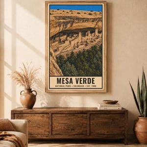 Pu&ograve; includere: Una stampa artistica da parete verticale con un'illustrazione dettagliata delle abitazioni rupestri di Mesa Verde in Colorado. L'opera mostra strutture in pietra color sabbia incastonate sotto una sporgenza rocciosa, alberi verdi e un cielo blu brillante, con il testo MESA VERDE NATIONAL PARK COLORADO EST. 1906.