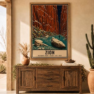 May include: A vertical wall art print featuring a stylized illustration of Zion National Park with red canyon walls, a blue river, and a tree decorated with colorful lights. The text reads ZION NATIONAL PARK UTAH EST. 1919 at the bottom.