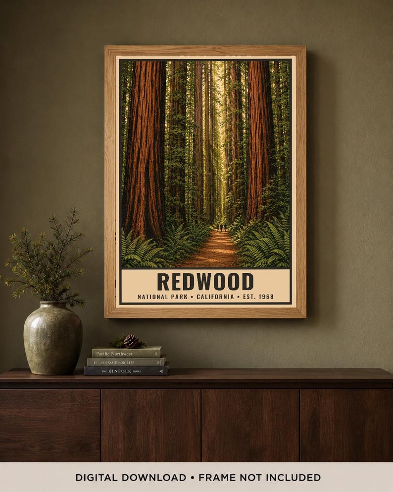 May include: A vertical rectangular poster in a light wood frame featuring a forest scene with tall redwood trees, green ferns, and a dirt path. The text at the bottom reads REDWOOD NATIONAL PARK &bull; CALIFORNIA &bull; EST. 1968 in black capital letters.