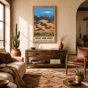 K&ouml;nnte beinhalten: Ein vertikaler Wandkunstdruck mit einer Landschaftsillustration des Great Sand Dunes Nationalparks in Colorado. Das Kunstwerk zeigt goldene Sandd&uuml;nen, dunkelgr&uuml;ne Berge und einen blauen Himmel mit einer Wolke. Der Text lautet: GREAT SAND DUNES NATIONAL PARK &bull; COLORADO &bull; EST. 2004.