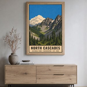 Op de afbeelding: Een verticale poster met een landschapsillustratie van het North Cascades National Park in Washington, opgericht in 1968. Het kunstwerk toont grillige bergtoppen, een diepe vallei en groenblijvende bomen onder een blauwe lucht.