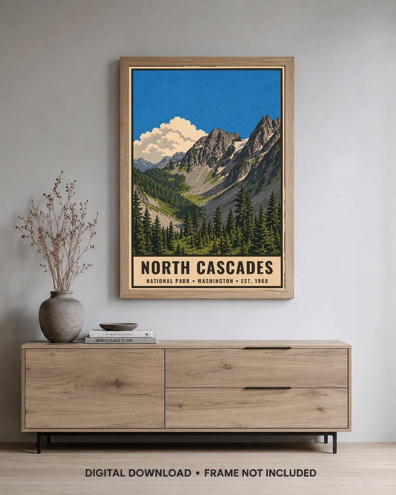 Op de afbeelding: Een verticale poster met een landschapsillustratie van het North Cascades National Park in Washington, opgericht in 1968. Het kunstwerk toont grillige bergtoppen, een diepe vallei en groenblijvende bomen onder een blauwe lucht.