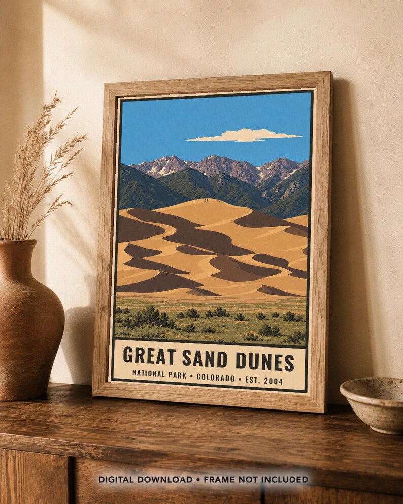 K&ouml;nnte beinhalten: Ein gerahmtes Poster mit einer stilisierten Illustration des Great Sand Dunes Nationalparks in Colorado. Das Kunstwerk zeigt goldene Sandd&uuml;nen, gr&uuml;ne Vegetation und schneebedeckte Berge unter einem blauen Himmel mit Text am unteren Rand.