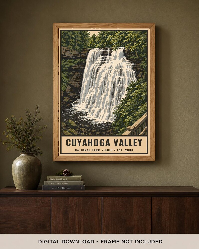Może przedstawiać: Oprawiony wydruk ścienny przedstawiający wodospad w Parku Narodowym Cuyahoga Valley w Ohio, założonym w 2000 roku. Ilustracja ukazuje kaskadę wodną otoczoną zielonymi drzewami, skalistymi klifami i drewnianą barierką w jasnej drewnianej ramie.