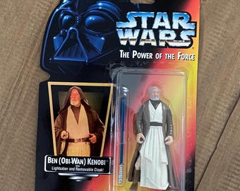 May include: A Star Wars action figure of Ben (Obi-Wan) Kenobi from The Power of the Force series. The figure is wearing a brown robe and a white tunic. He is holding a blue lightsaber. The figure comes with a removable cloak.