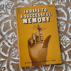 May include: A yellow paperback book titled "10 Days to a Successful Memory" with an illustration of a wooden hand with a string tied around one finger. The book is abridged and by Joyce Brothers, Ph.D. & Edward P. F. Eagan.