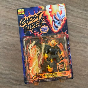 Może przedstawiać: Plastikowa figurka Ghost Ridera, superbohatera z komiksów Marvela, na motocyklu. Figurka jest ubrana w czarny i pomarańczowy strój z płonącą czaszką. Figurka jest zapakowana w plastikowe opakowanie blister z dołączonym komiksowym zeszytem. Opakowanie zawiera logo Marvel Comics i napis "Ghost Rider" dużymi, pogrubionymi literami.