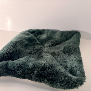 May include: A square-shaped, dark forest green fabric accessory with a soft, plush, and fuzzy texture. The item features a distinct cross-stitched seam pattern across the center, creating four slightly raised, padded sections in a quilted style.