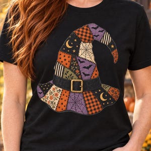 May include: A black short-sleeve t-shirt featuring a large graphic of a patchwork witch hat. The hat design includes various patterns such as orange and black plaid, purple fabric with bats, spider webs, crescent moons, and floral prints.