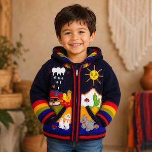 Peut inclure: Un sweat à capuche zippé en tricot bleu marine orné de motifs brodés colorés, notamment un soleil jaune, un nuage de pluie blanc, un oiseau jaune, un cactus vert et des petits animaux. Les manches et la capuche présentent des rayures arc-en-ciel.
