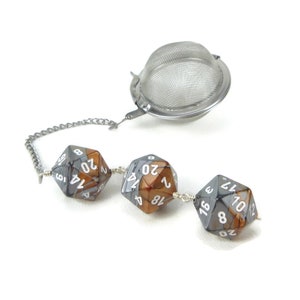 May include: A silver tea infuser with a chain attached to three silver and brown dice. The dice are numbered 1-20.