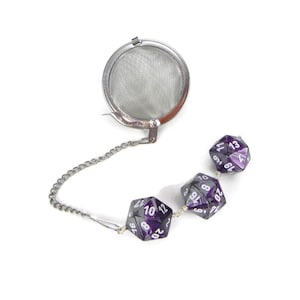 May include: A silver tea infuser with a chain and three purple and white dice attached to it.