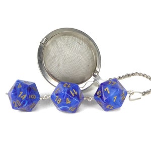 May include: A silver tea infuser with a chain and three blue dice with gold numbers. The dice are connected to the chain.