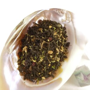 May include: A close-up of a mixture of black tea leaves, herbs, and dried fruit in a white seashell. The tea blend is a mix of black tea, dried fruit, and herbs.