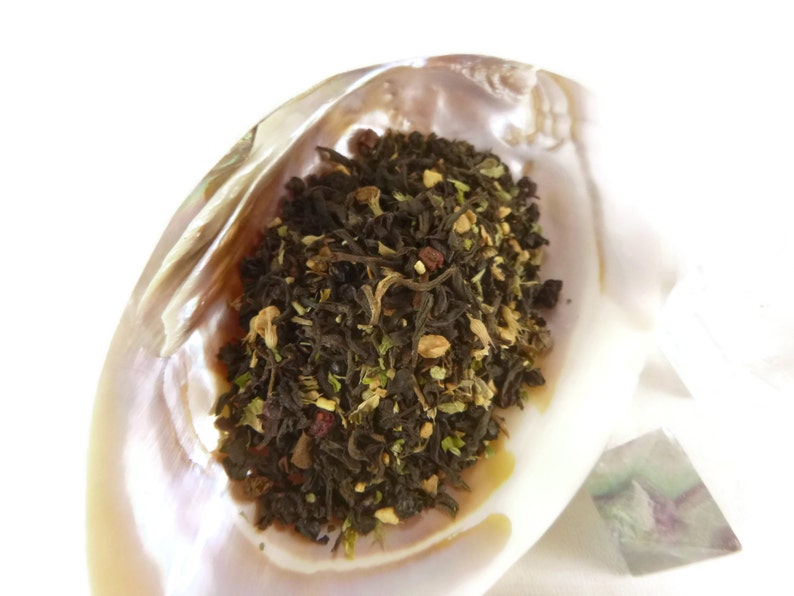 May include: A close-up of a mixture of black tea leaves, herbs, and dried fruit in a white seashell. The tea blend is a mix of black tea, dried fruit, and herbs.