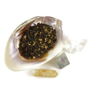 May include: A seashell filled with loose leaf tea, surrounded by three crystals: a clear quartz, a green fluorite, and a yellow citrine.