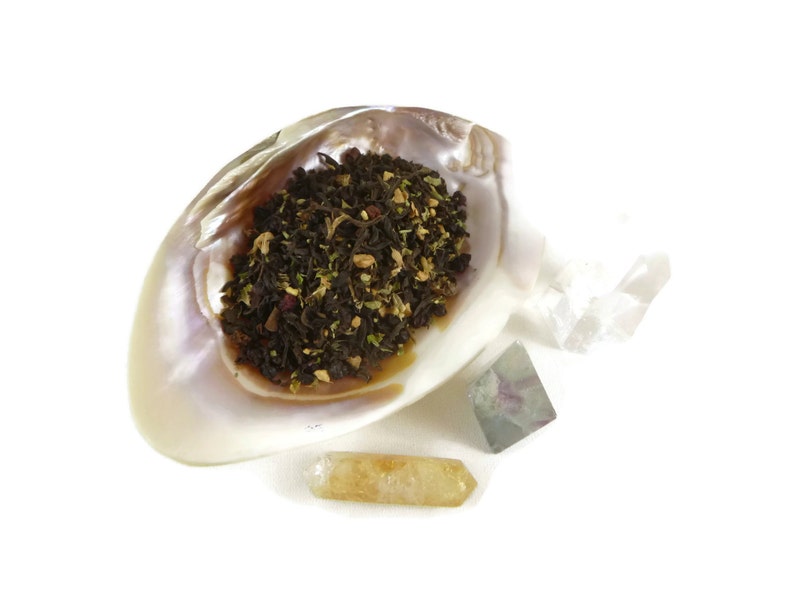 May include: A seashell filled with loose leaf tea, surrounded by three crystals: a clear quartz, a green fluorite, and a yellow citrine.