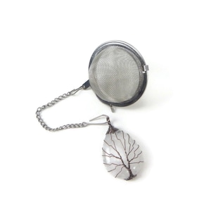 May include: A silver tea infuser with a chain and a clear quartz crystal with a copper wire tree design.