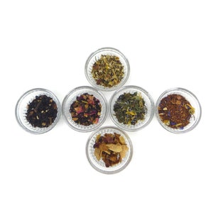 May include: Six small glass bowls filled with different types of loose leaf tea. The tea blends include black tea, green tea, herbal tea, and fruit tea.
