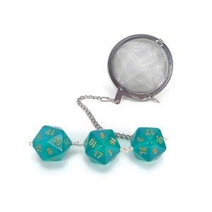 May include: A teal green tea infuser with a metal chain and a round mesh strainer. The chain is attached to three teal green dice with gold numbers.