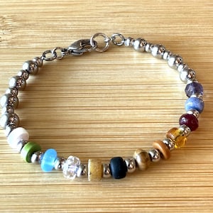 May include: A bracelet featuring a series of metallic silver-toned spherical beads interspersed with a variety of colorful, multi-textured beads including shades of white, green, light blue, clear, yellow, black, brown, amber, deep red, and dark purple.